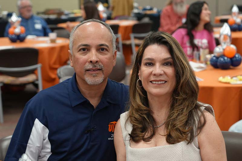 Group of attendees pose together during a UTEP Engineering homecoming gathering while holding a large “Civil Engineering” banner, with participants seated and standing in front of a backdrop decorated with orange, blue, silver, and black balloons and star-shaped accents.